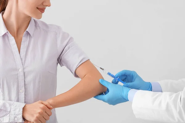 Doctor vaccinating young woman on light background — Stock Photo, Image