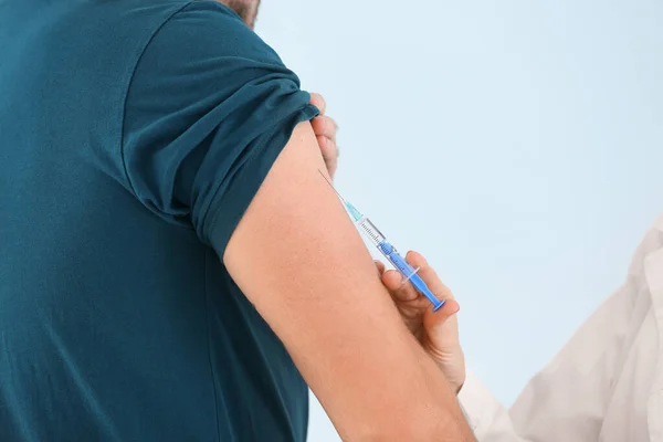 Doctor vaccinating young man on light background, closeup