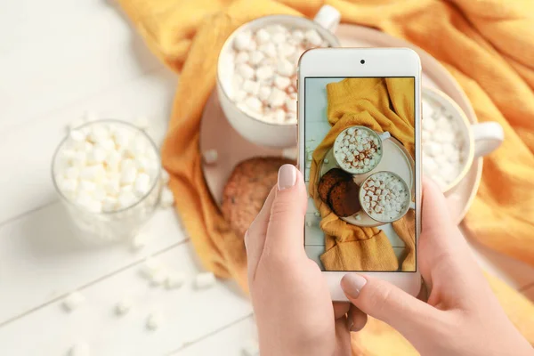 Kobieta fotograf żywności z telefonem komórkowym robi zdjęcie gorącej czekolady z piankami — Zdjęcie stockowe