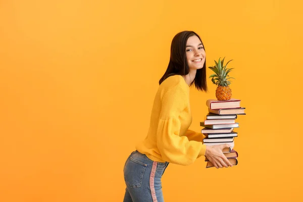 Beautiful young woman with books and pineapple on color background — 스톡 사진