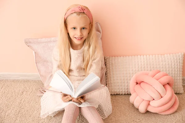 Маленька дівчинка читає книгу біля кольорової стіни — стокове фото