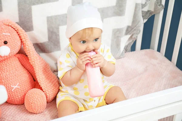 Niedliches Baby trinkt Milch aus der Flasche in der Krippe — Stockfoto