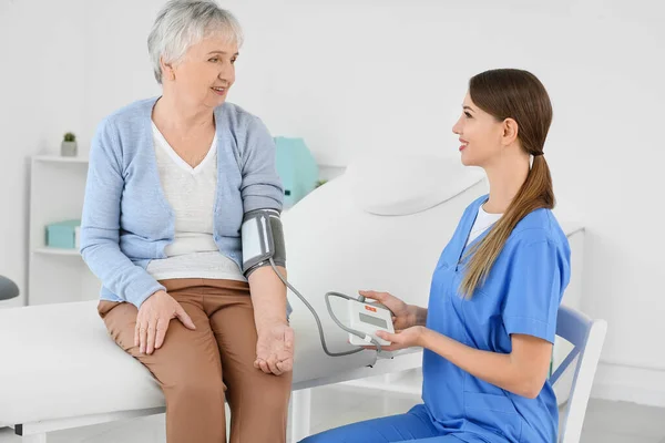 Doctora que mide la presión arterial de una mujer mayor con síndrome de Parkinson en la clínica —  Fotos de Stock