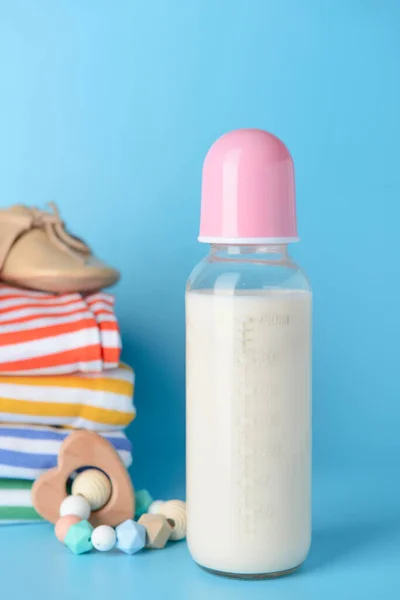 Bottle of milk for baby with clothes on color background — Stock Photo, Image