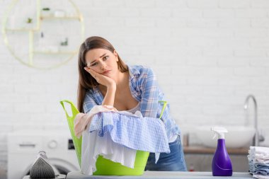 Tired housewife with laundry at home