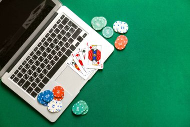 Chips and playing cards for gambling games with laptop on color background