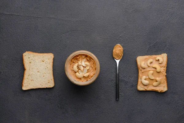 Tarro de mantequilla de anacardo con pan sobre fondo oscuro — Foto de Stock