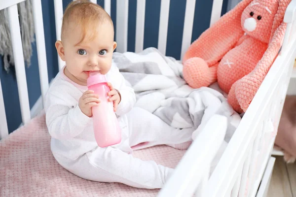 Мила дитина п'є молоко з пляшки в ліжечку — стокове фото