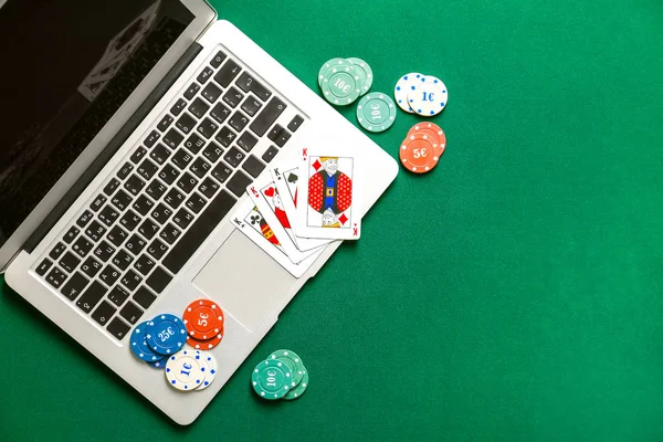 Chips and playing cards for gambling games with laptop on color background — Stockfoto