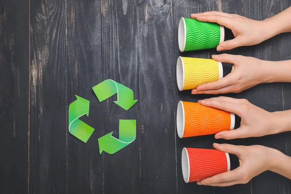 Hände mit gebrauchten Tassen auf dunklem Holzgrund. Recyclingkonzept — Stockfoto