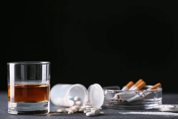 Glass of whiskey with cigarettes and drugs on table against dark background — Stok fotoğraf