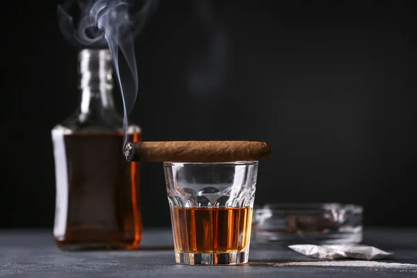 Glas whisky met sigaar op tafel tegen donkere achtergrond. Begrip alcoholisme — Stockfoto