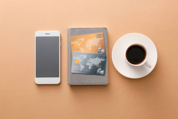 Cartões de crédito com telefone celular e xícara de café no fundo de cor. Conceito de banco online — Fotografia de Stock