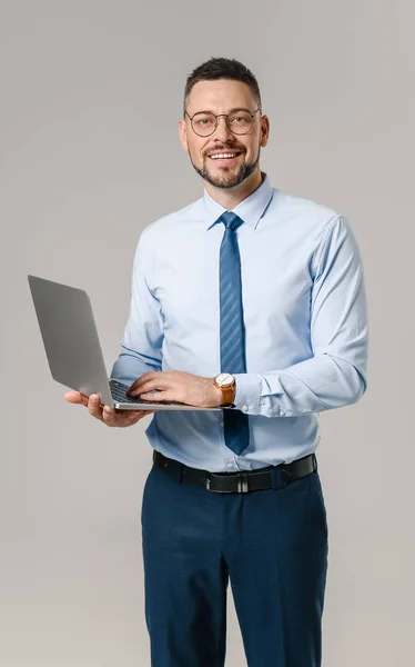 Portrait of handsome businessman with laptop on grey background — Stock Photo, Image