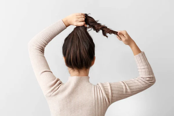 Young woman doing her hair on light background — Stock Photo, Image