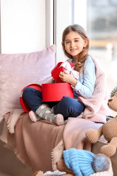 Cute little girl with gifts on window sill at home — Stock Photo, Image