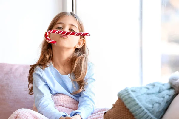 Cute little girl with Christmas candy cane on window sill at home — Stock Photo, Image