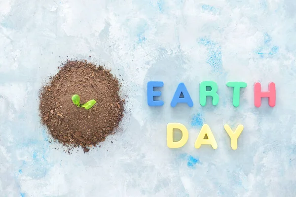 Heap of soil with plant and text EARTH DAY on color background — Stock Photo, Image