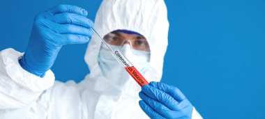 Laboratory worker in protective uniform and with sample of Coronavirus in test tube on color background