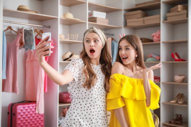 Beautiful young women taking selfie in room with large wardrobe
