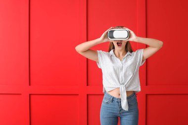 Young woman with VR glasses against color wall