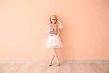 Little girl with books near color wall