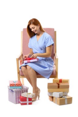 Bir sürü hediye kutusu olan güzel bir kadın beyaz arka planda koltukta oturuyor.
