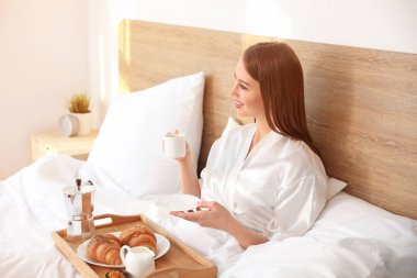 Güzel genç bir bayanın yatakta kahvaltı ettiği bir sabah.