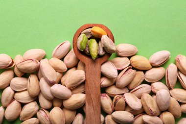 Spoon and tasty pistachio nuts on color background