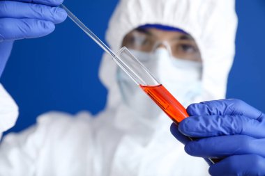 Laboratory worker in protective uniform and with sample in test tube on color background. Concept of epidemic