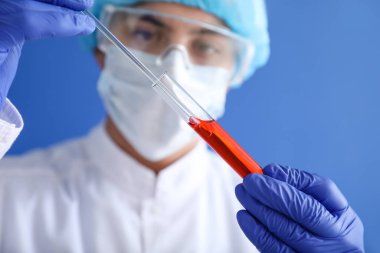 Laboratory worker in protective uniform and with sample in test tube on color background. Concept of epidemic