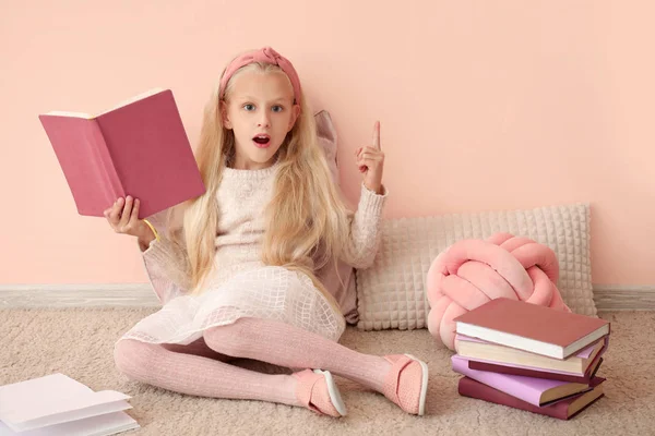 Little girl with raised index finger and book near color wall — Stok fotoğraf