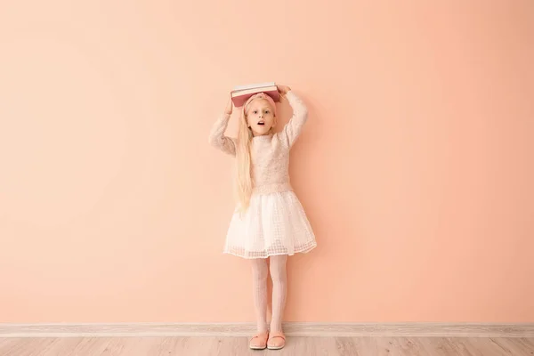 Kleines Mädchen überrascht mit Büchern in der Nähe der Farbwand — Stockfoto