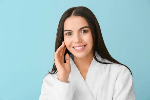 Beautiful young woman in bathrobe on color background — Stock Photo, Image