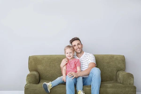 Счастливые молодой отец и дочь сидят на диване возле светлой стены — стоковое фото