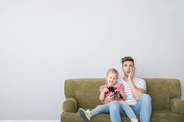 Fiatal apa és lánya videojátékozik, miközben ül a kanapén a fény háttér — Stock Fotó