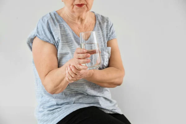 Старшая женщина, страдающая синдромом Паркинсона со стаканом воды в клинике — стоковое фото