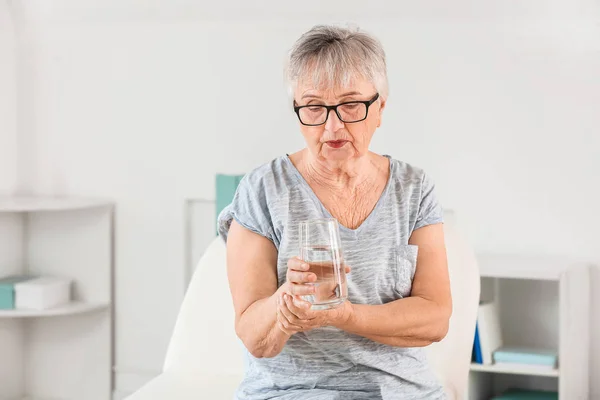 Старша жінка, яка страждає синдромом Паркінсона зі склянкою води в клініці — стокове фото