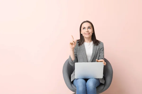 Young businesswoman with laptop and raised index finger on color background — Stok fotoğraf