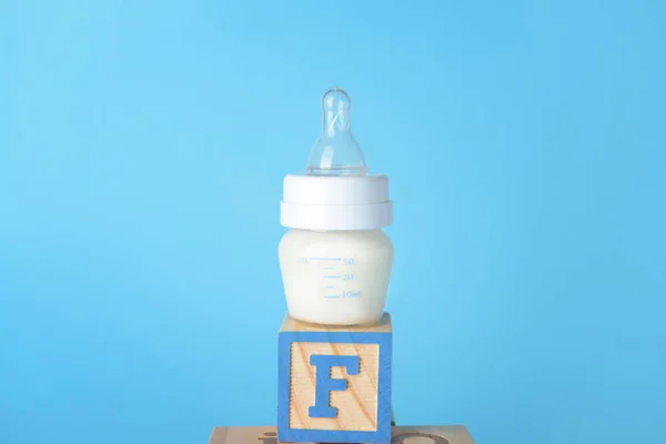 Bottle of milk for baby with cube on color background — Stock Photo, Image