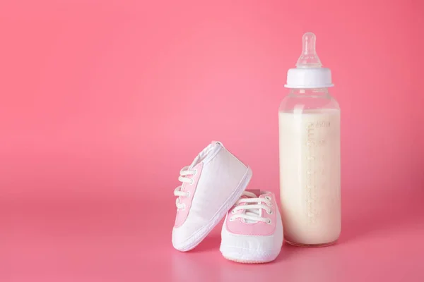 Bottle of milk for baby with shoes on color background — Stock Photo, Image
