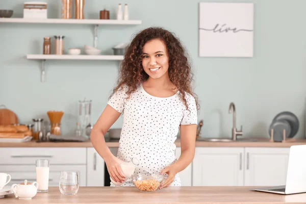 Mujer afroamericana embarazada con leche y copos en la cocina —  Fotos de Stock