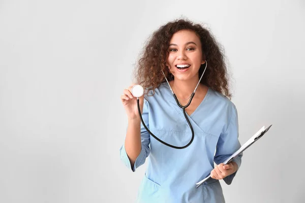 Młoda afroamerykańska pielęgniarka ze stetoskopem na jasnym tle — Zdjęcie stockowe