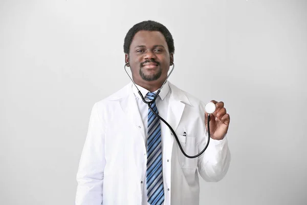 African-American doctor with stethoscope on light background — Stock Photo, Image