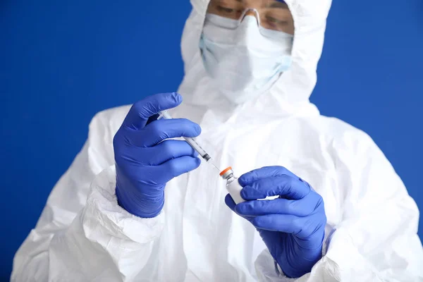 Laboratory worker in protective uniform and with vaccine on color background. Concept of epidemic — Stok fotoğraf