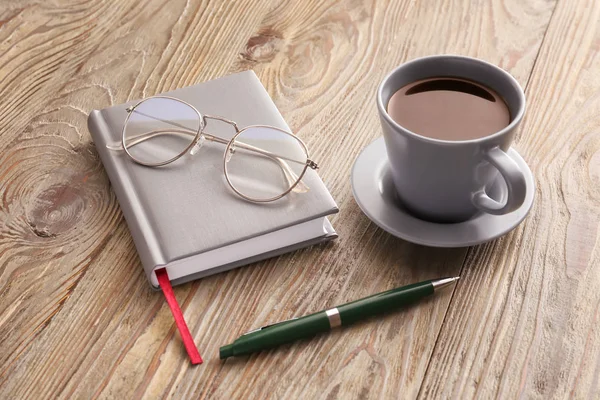 Notebook with cup of coffee, pen and eyeglasses on wooden table — Stock Photo, Image