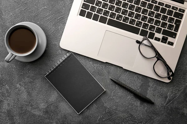 Laptop with cup of coffee, eyeglasses and stationery on dark background — Stock Photo, Image