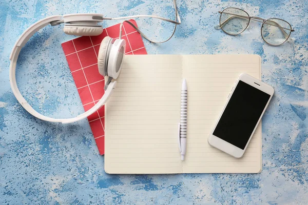 Notebooks with mobile phone, headphones and eyeglasses on color background — Stock Photo, Image