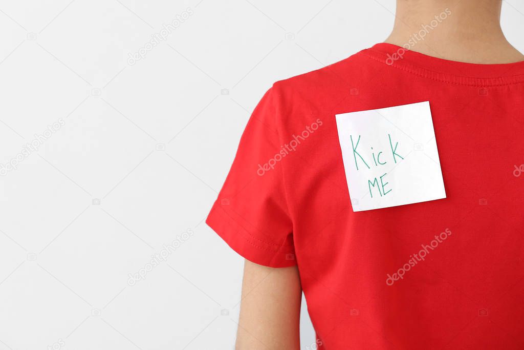 Sticky note with text KICK ME on back of little boy against light background. April Fools' Day celebration