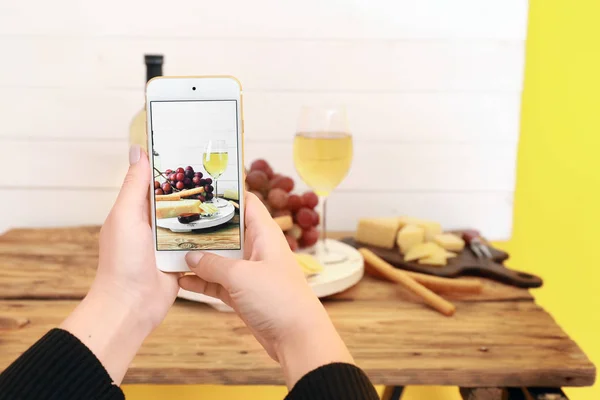 Female food photographer with mobile phone taking picture of cheese and wine